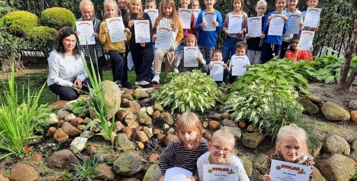 Grupowe zdjęcie dzieci trzymających dyplony, dookoła zieleń 