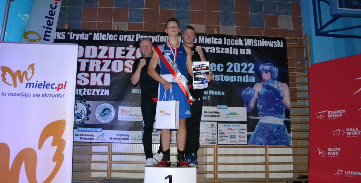 Zawodnik stojący na podium, za nim dwóch trenerów