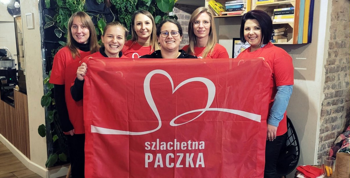 Sześć kobiet trzymających czerwoną flagę z napisem Szlachetna Paczka