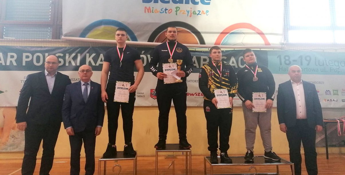 Zawodnicy z dyplomami na wspólnym zdjęciu na podium , obok trenerzy