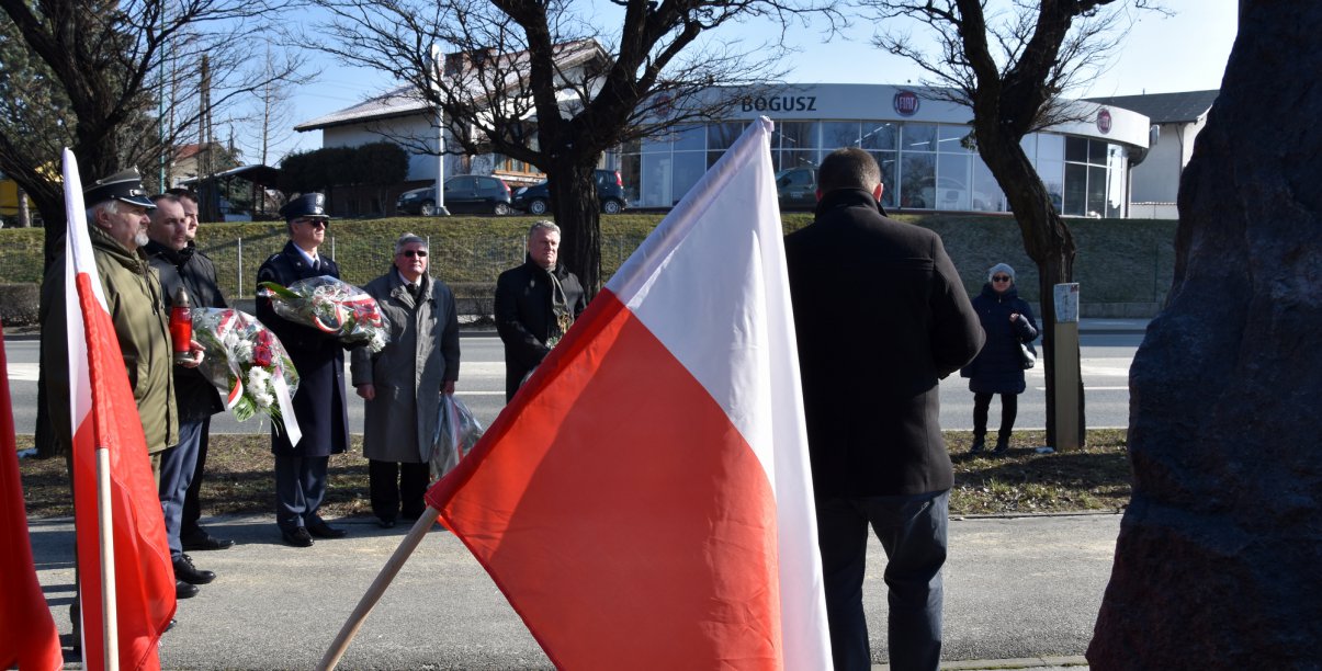 Falag Polski na pierwszym planie, w drugim pplanie grupa osób stojąca przy ulicy