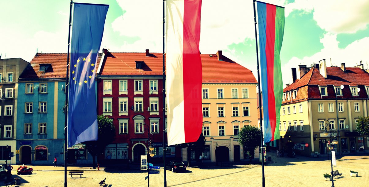 Flagi Unii Europejskiej, Polski i Dzierżoniowa na masztach, w tle kamienice