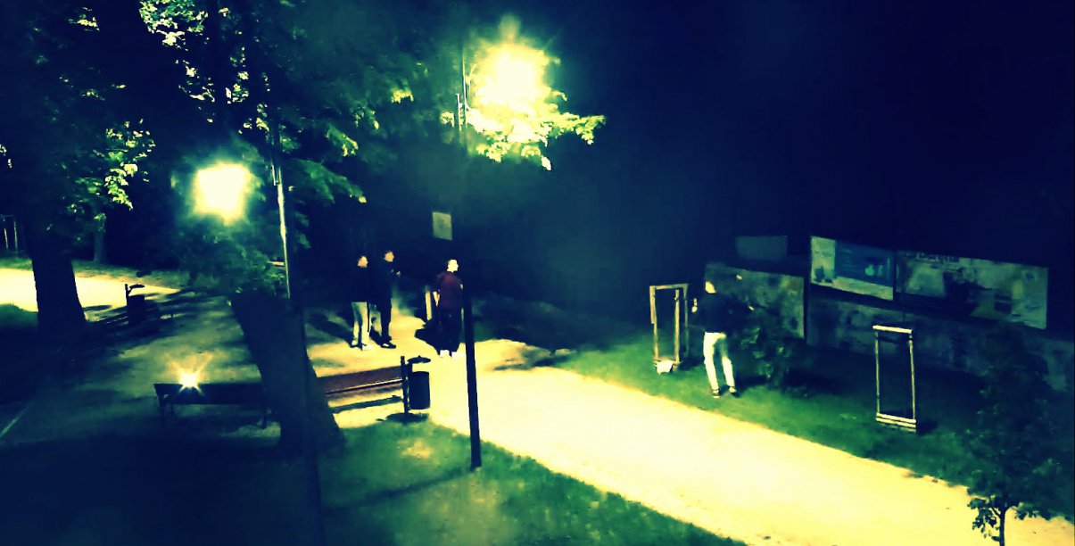 Park nocą, oświetlona alejka i grupka osób