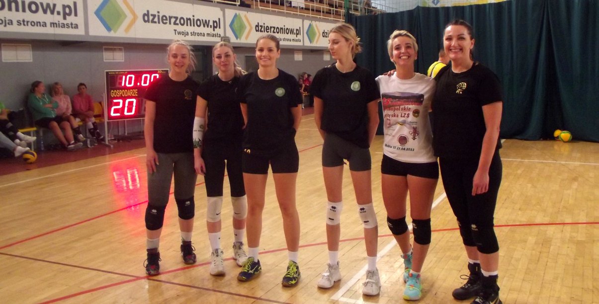Sześć usmiechniętych siatkarek na wspólnym zdjęciu w halisportowej, w tle reklama strony www.dzierzoniow.pl