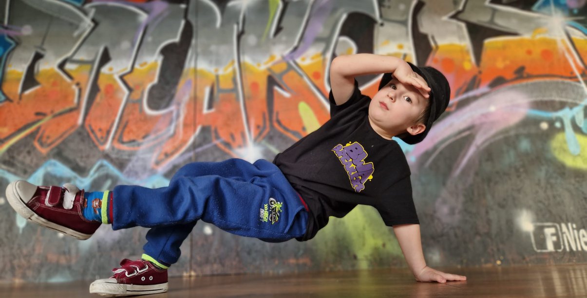 Młody chłopak tańczący breakdance, z tyłu graffitti