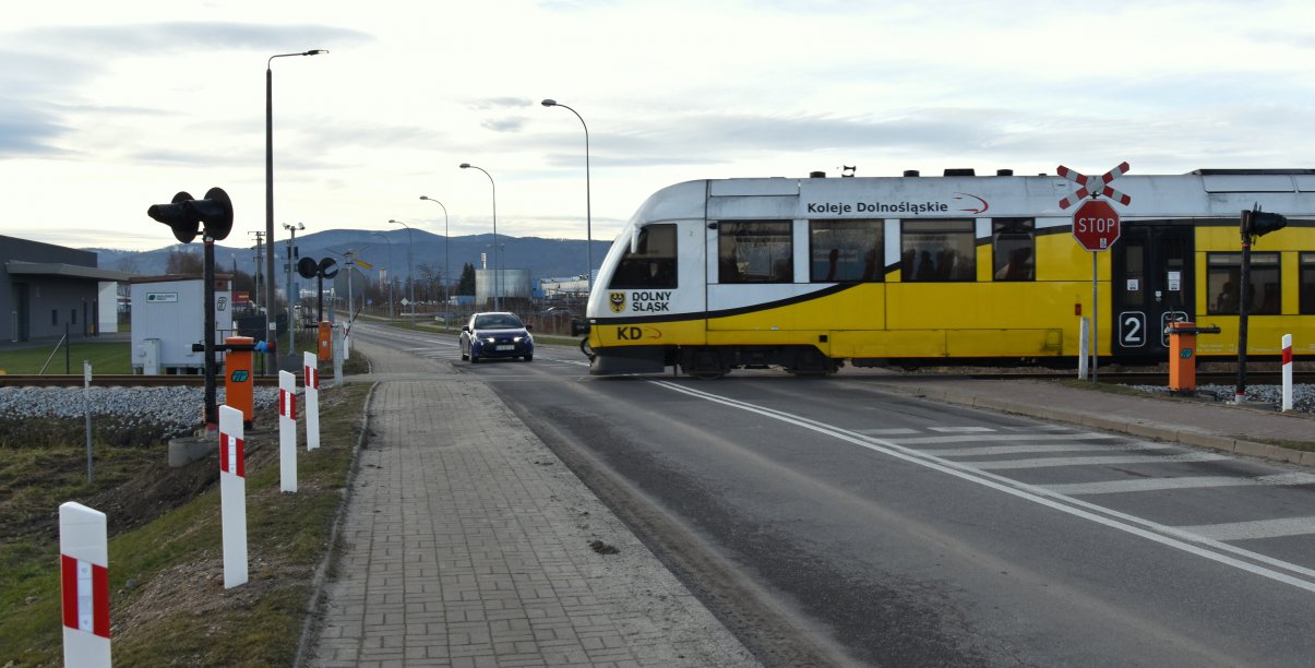 Szynobus, za nim samochód osobowy, w tle góry