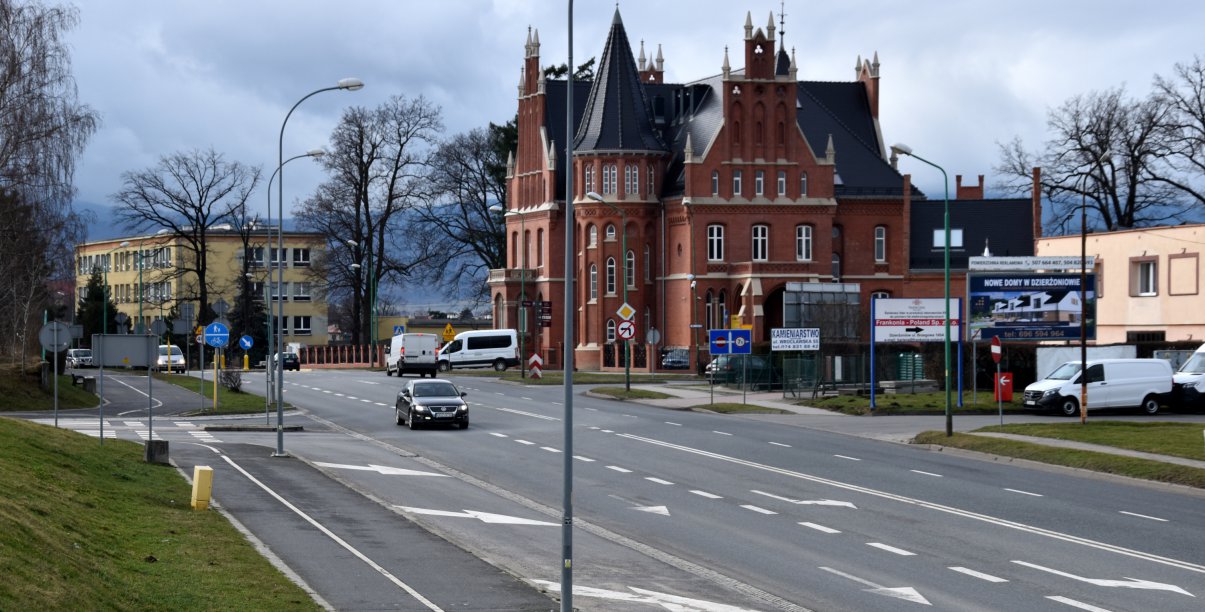 Szeroka droga, obok duża kamienica z czerwonej cegły