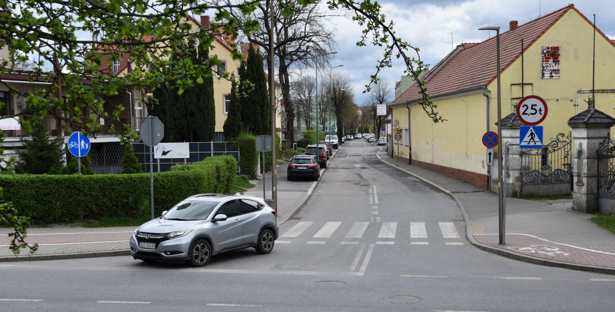 Skrzyżownie dróg, samochód włączający się do ruchu, po bokach zieleń i budynki