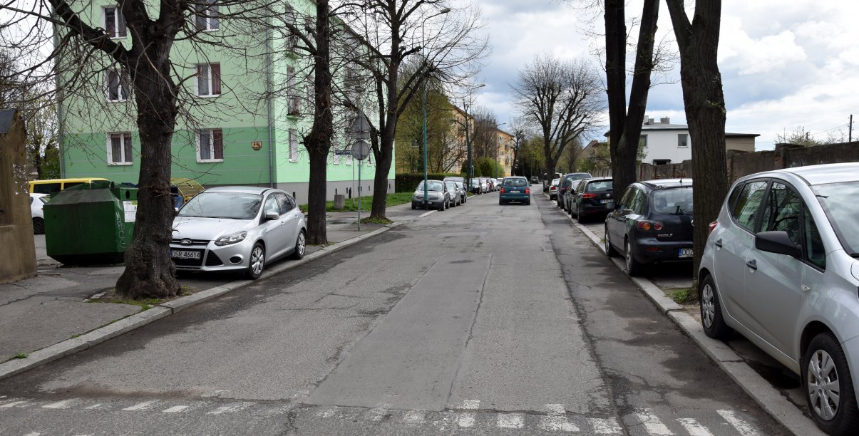 Droga asfaltowa, na chodnikach zaparkowane samochody