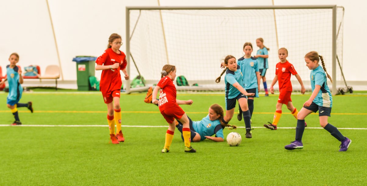 Młode dziewczyny w sportowych strojach grają w piłkę, w tle bramka