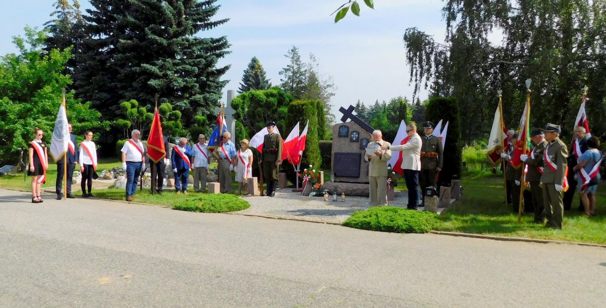 Cmentarny obelisk, ludzie z flagami Polski, żołenierze i kombatanci w mundurach 