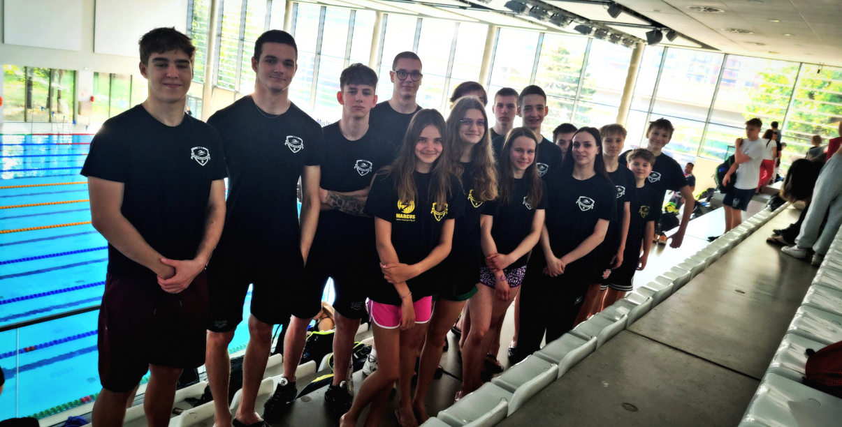 Młodzi pływacy w czarnych koszulkach stoją przy krawędzi basenu