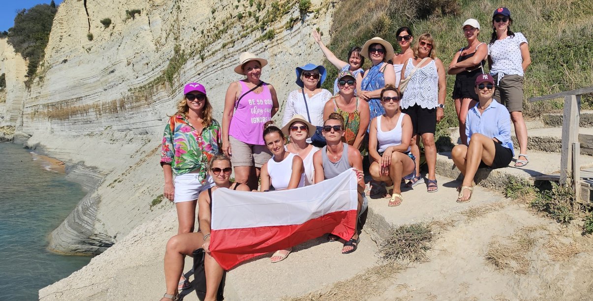 Grupa kobiet na kamenistej plaży, jedna z pań trzyma flagę Polski