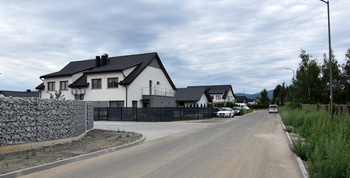 Ulica na osiedlu domków jednorodzinnych, Duży, biały dom, obok kamienny mur