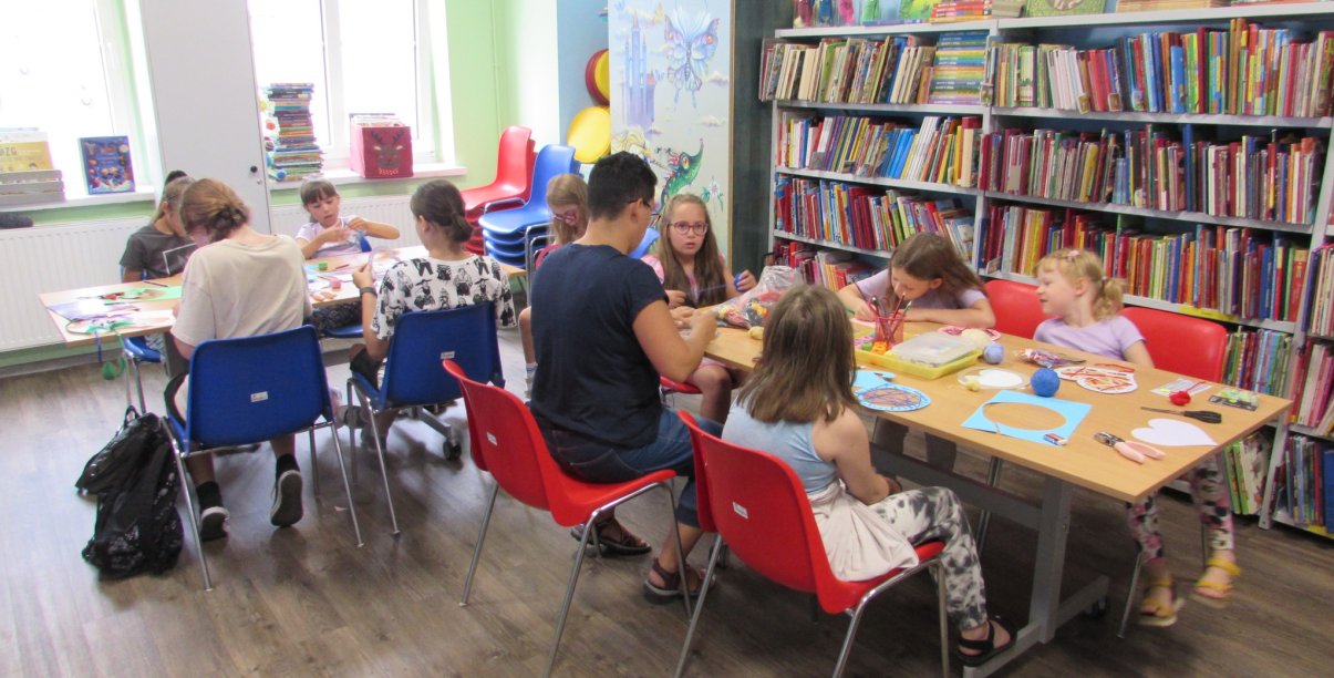 Grupa dzieci maluje przy dwóch stołach w bibliotece