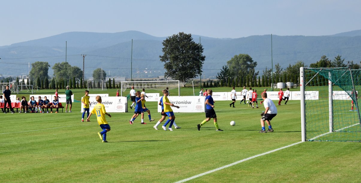 Mecz piłki nożnej, trawiaste boisko. zawodnicy w żółtych i błękitnych strojach, w tle panorama gór