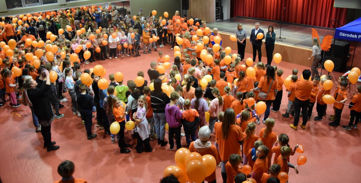 Ponad sto dzieci z pomarańczowymi balonamu w rękach ustawionych w symbol wstążki