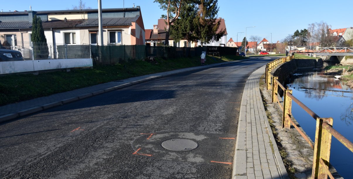 Droga asfaltowa, po lewej stronie rzeka, po prawej budynki