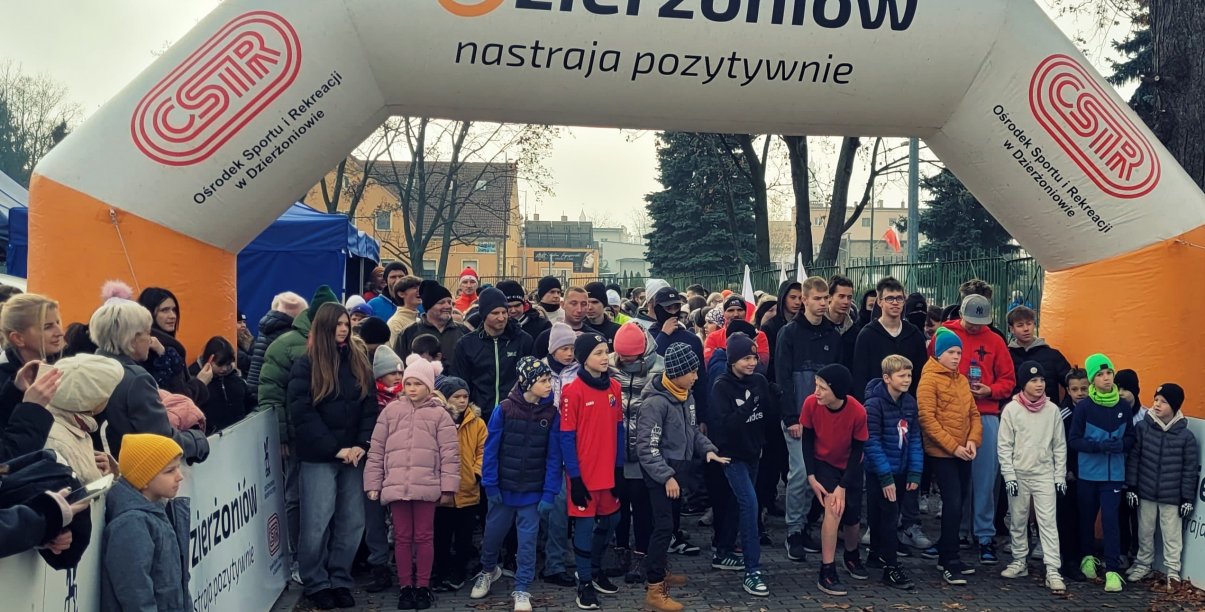 Kilkadziesiąt osób w róznym wieku na starcie wyścigu, u góry napis Dzierżoniów Nastraja Pozytywnie