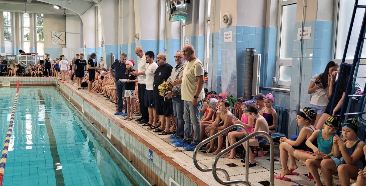 Dzieci siedzące przy krawędzi basenu krytego przed zawodami sportowymi