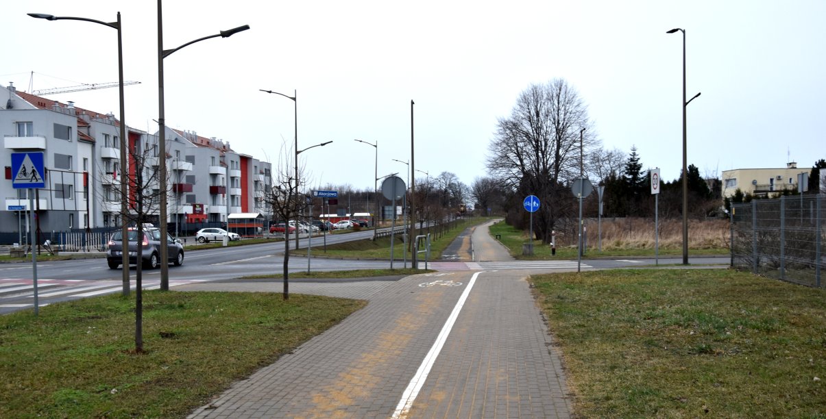 Szeroka ścieżka rowerowa przy drodze wyjazdowej z miasta, po lewej bloki mieszkalne