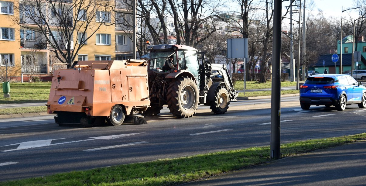 Maszyna zamiataqjąca drogę w mieście podczas ruchu samochodów