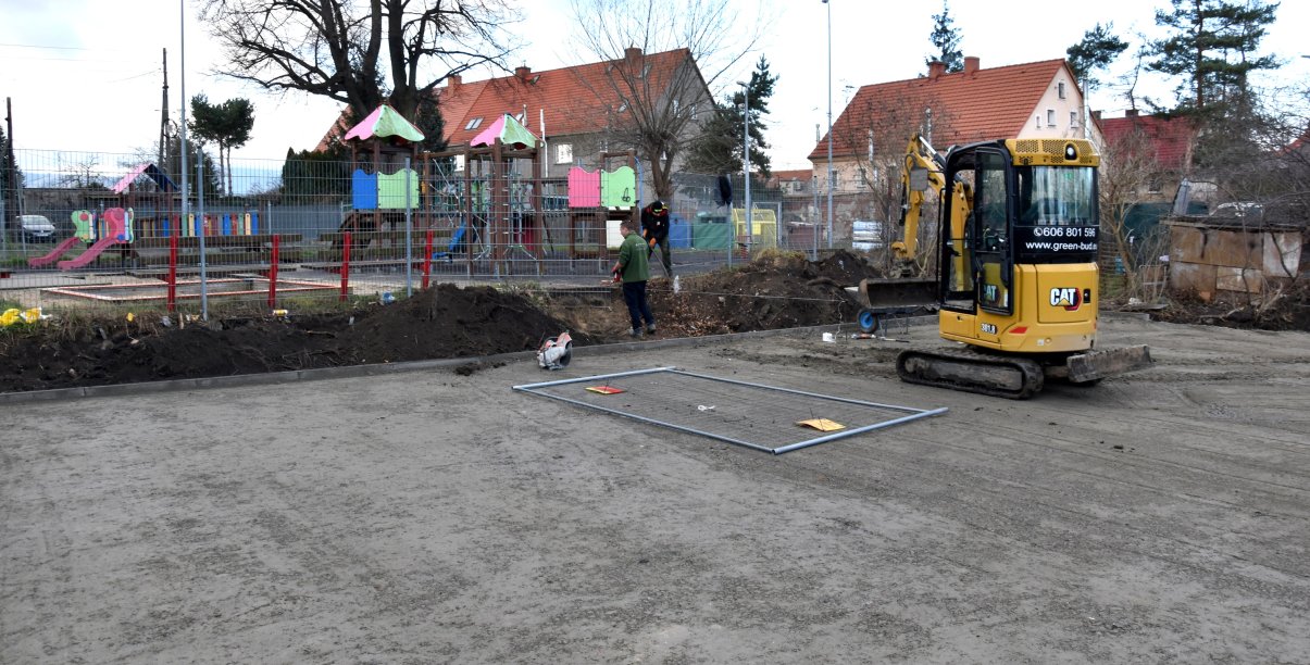 Utwardzony teren pod boisko do koszykówki, w tle plac zabaw i budynki mieszkalne