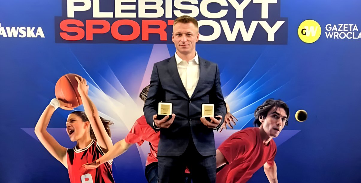 Patryk Ciszewski ze statuetkami w dłoniach, za nim napis Plebiscyt Sportowy