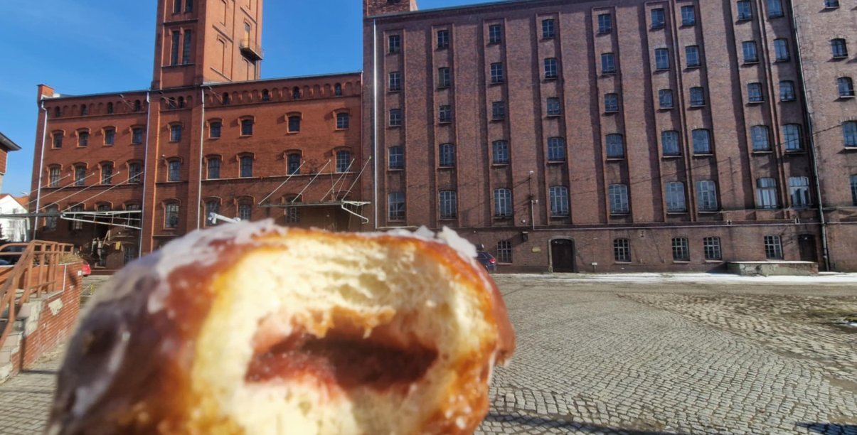 Nagryziony pączek, w tle budynek Młyna Hilberta z czerwonej cegły