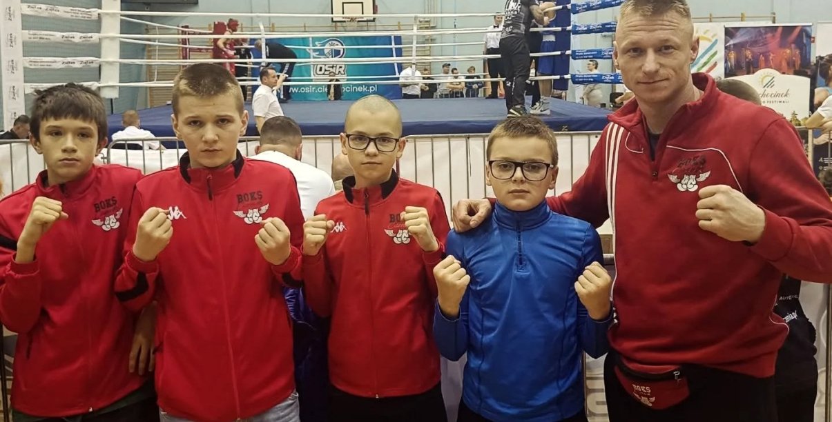 Czwórka zawodników i trener na wspólnym zdjęciu, z tyłu ring