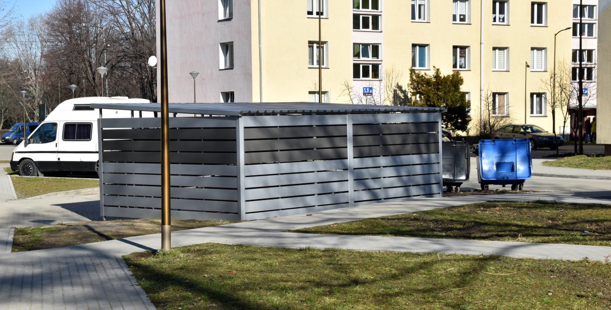 Zadaszony boks na śmieci zbudowny z szarych płyt ażurowych