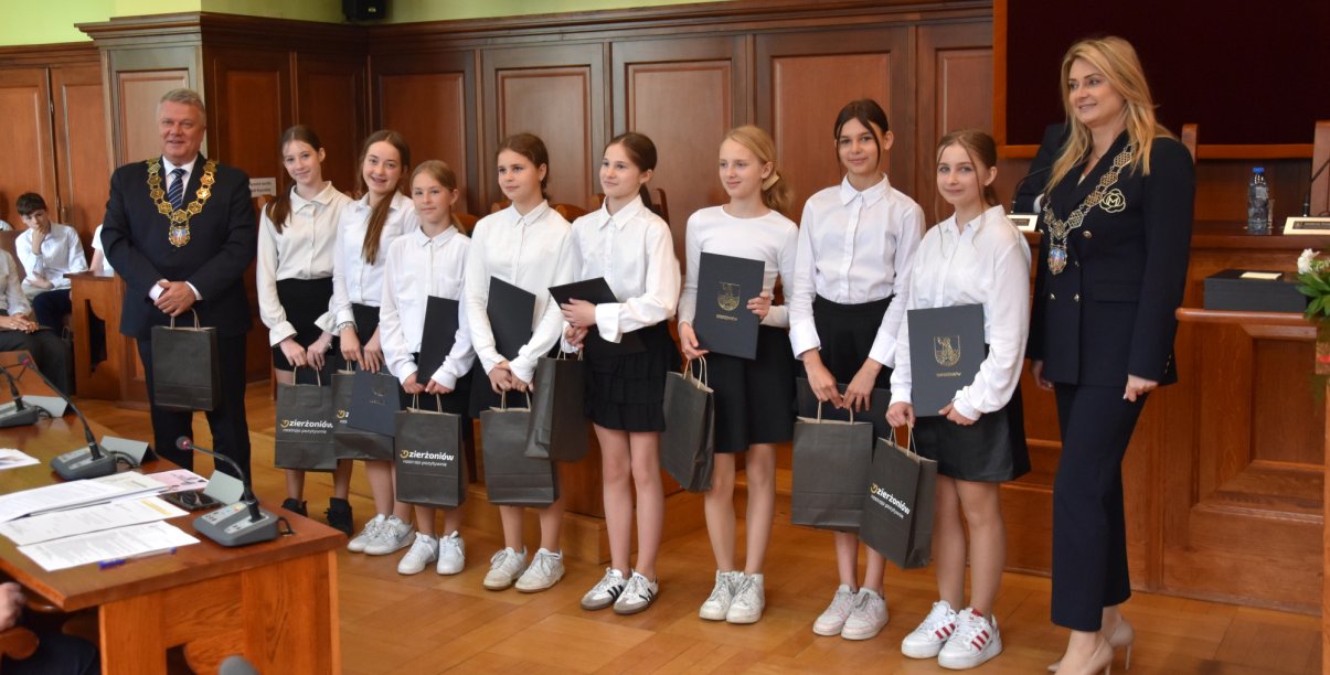 Uczennice w białych koszulach z dyplomami w rękach, obok burmsitrz i przewodnicząca Rady Miejskiej Dzierżoniowa
