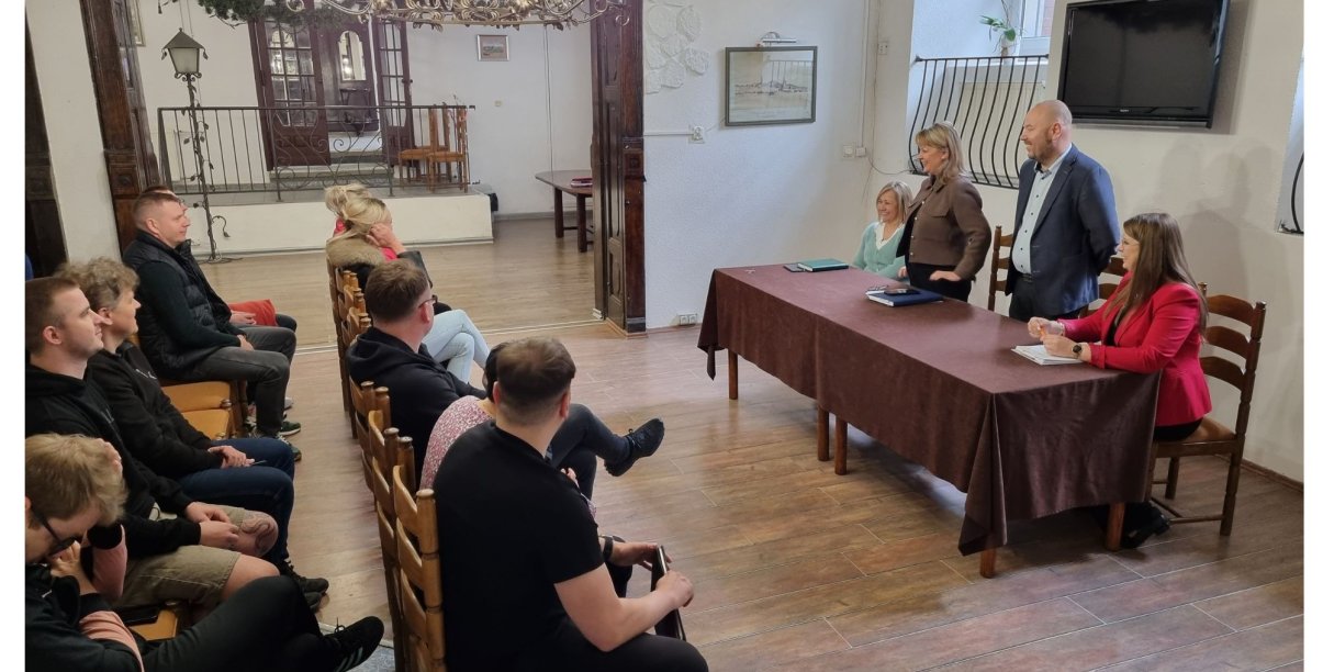 Grupa osób siedzi na krzesłach podczas spotkania.