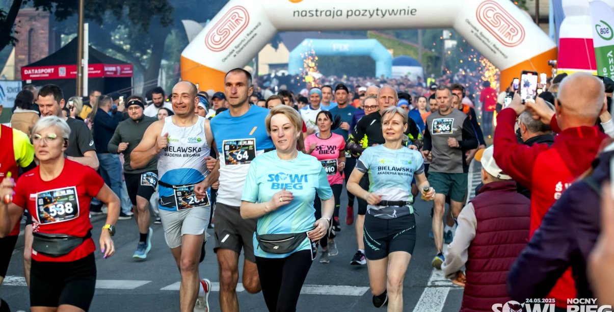 Ulica zapełniona biegaczami w sportowych strojach, za nimi napis Dzierżoniów