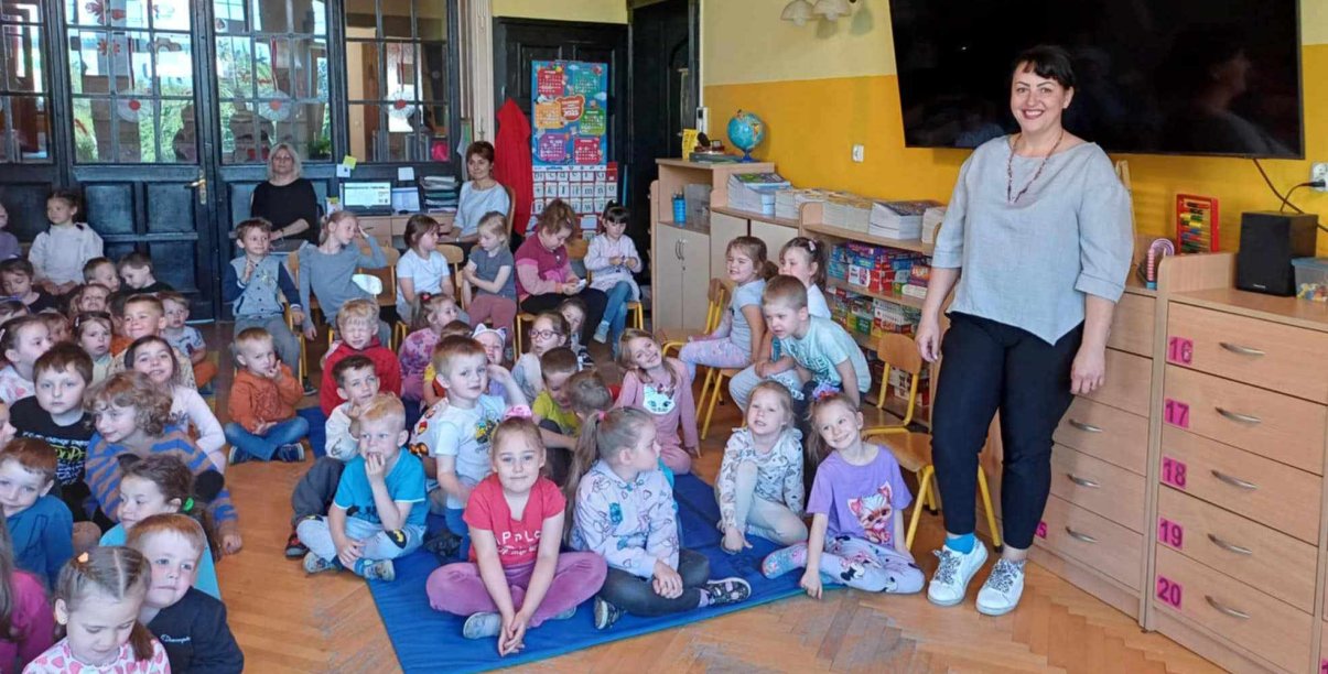 Grupa przedszkolaków siedzących na podłodze w dużym pomieszczeniu