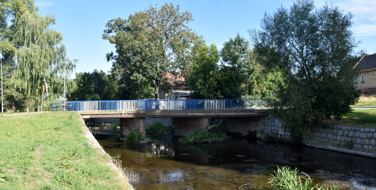 Most nad rzeką Piławą, po bokach i za mostem duże drzewa