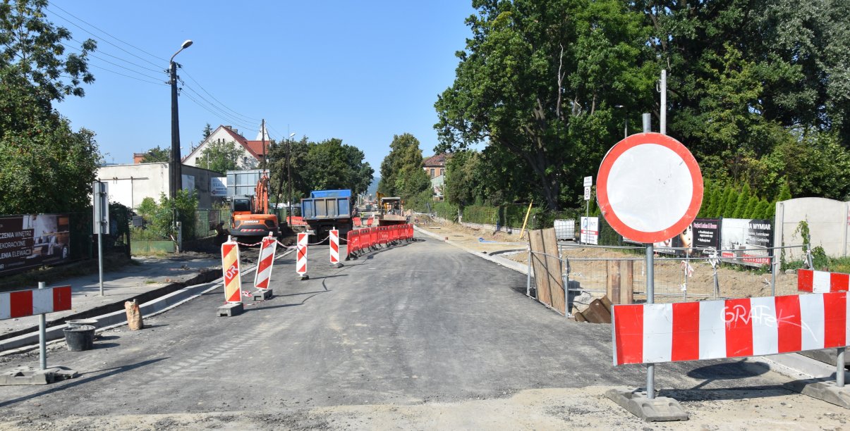 Droga w czasie remontu, poustawiane znaki ostrzegawcze, w tle auta ciężarowe i maszyny budowlane