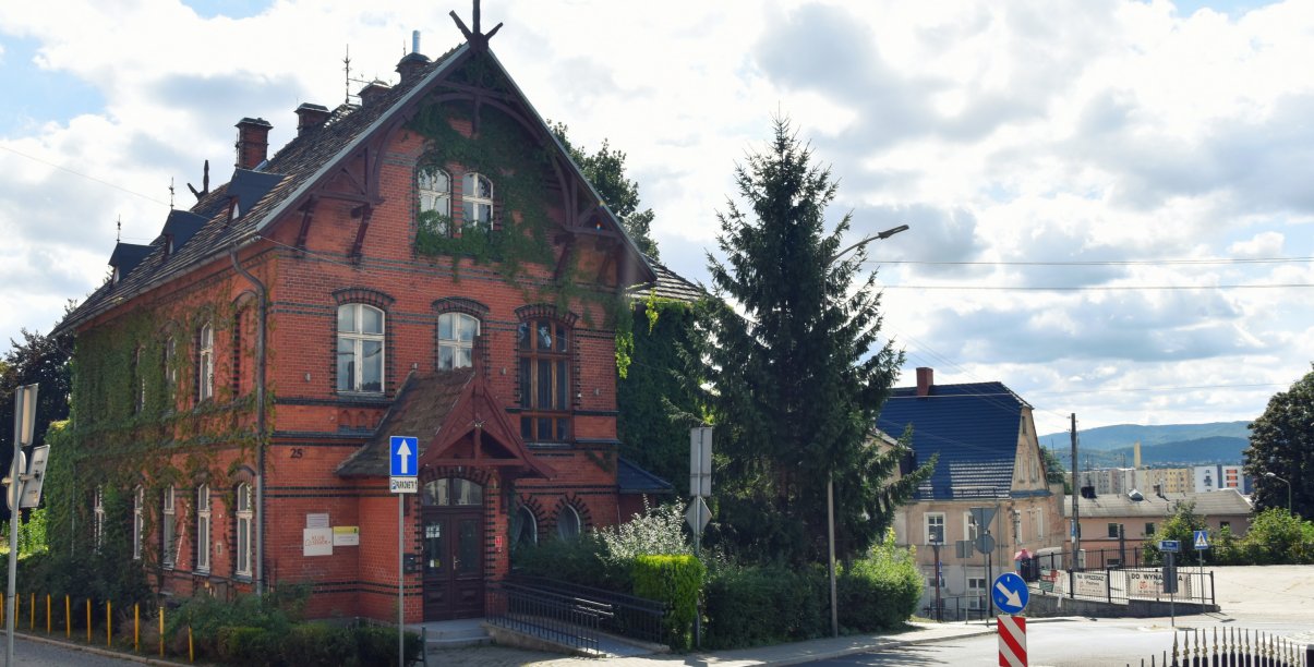 Zabytkowa kamienica z czerwonej cegły, jedna ze ścian częściowo porośnieta bluszczem