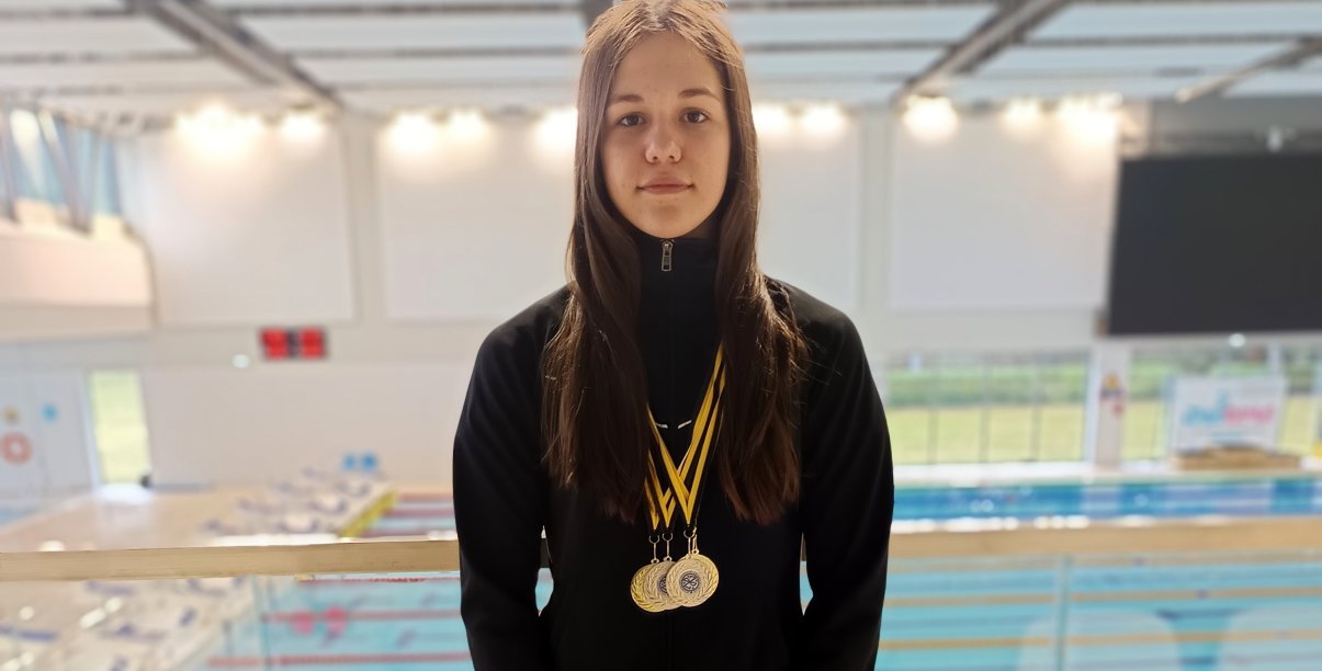 Natasza Paraciej z medalami na szyi przy niecce basenu krytego