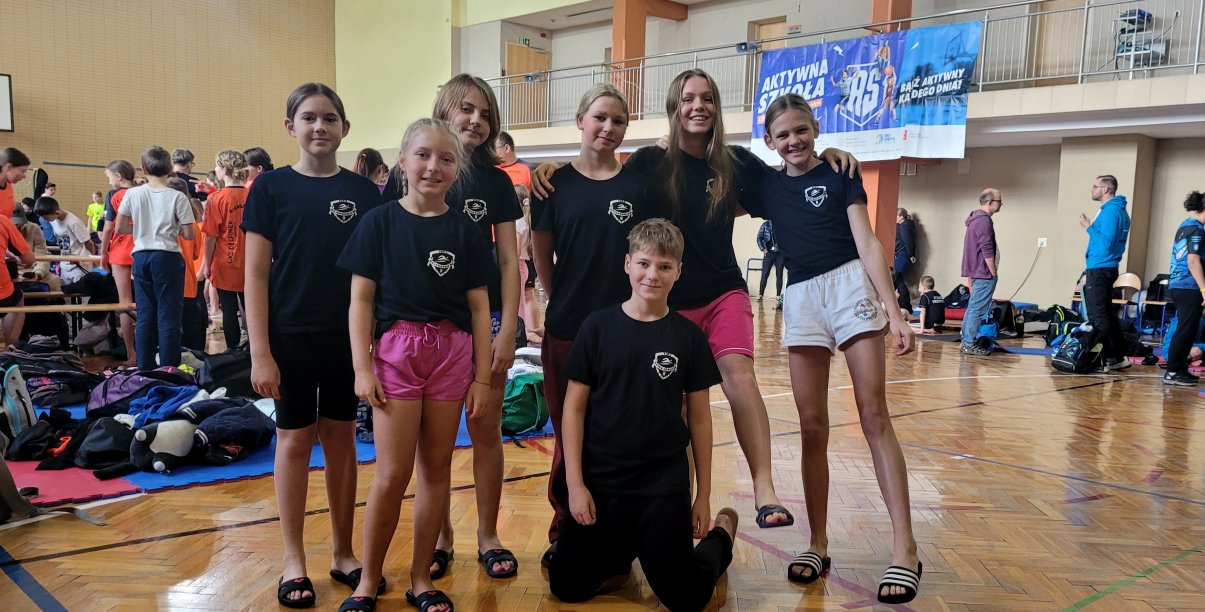 Grupa dzieci w koszulkach klubu MKS 9 na sali gimnastycznej