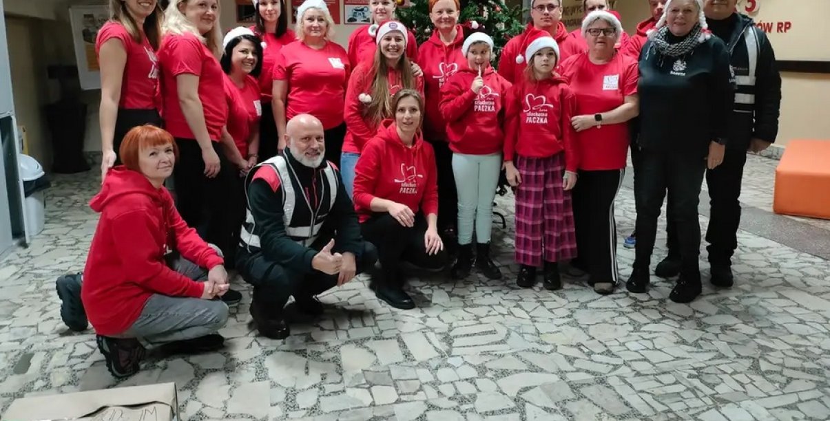 Grupa wolontariuszy Szlechetniej paczki w czerwonych koszulkach i czapkach św. Mikołaja stoi w korytarzu Zespołu Szkół nr 3 w Dzierżoniowie