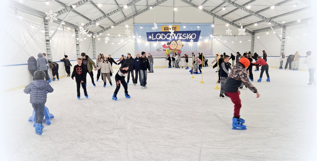 Wnętrze namiotu z lodowiskiem, na tafli lodowiska łyżwiarze w różnym wieku