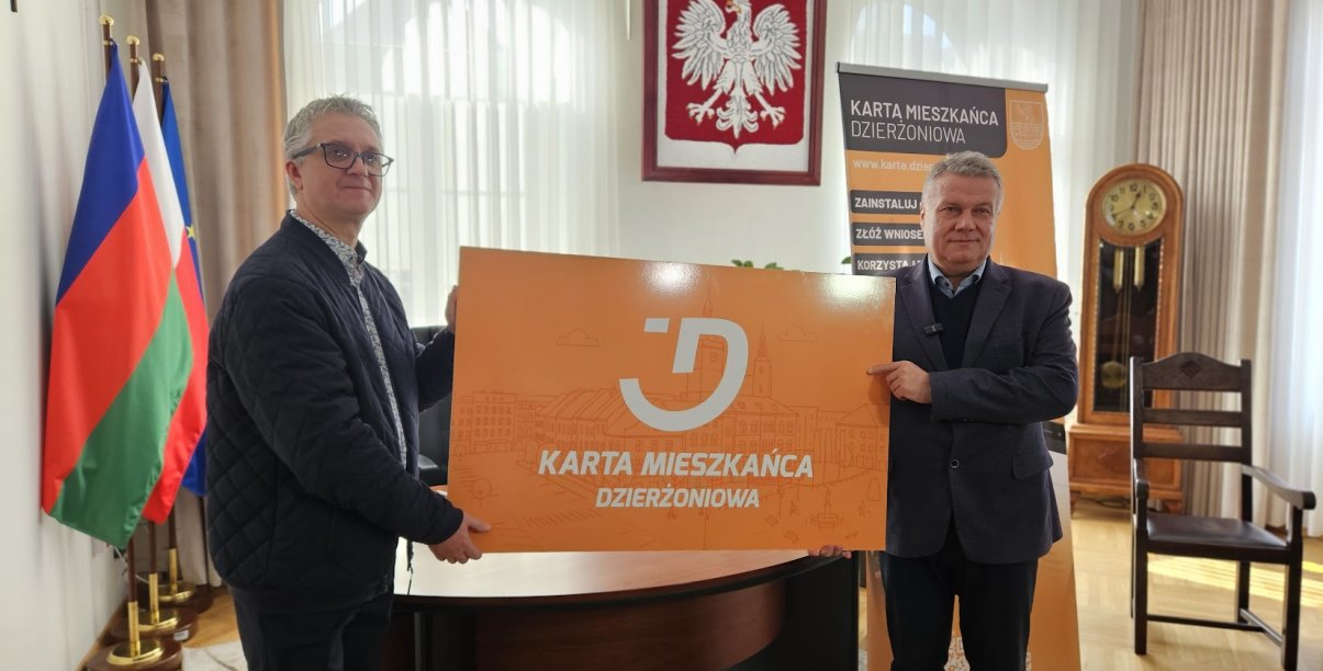 Mieszkaniec dzierzoniowa oraz burmistrz trzymają duża plastikową pomarańczową kartę meiszkańca
