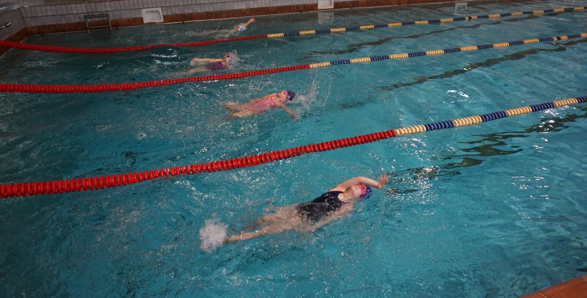 dzieci pływające na basenie grzbietem