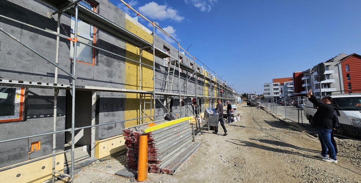 Budynek szeregowy w trakcie budowy, na drugim planie pracownicy przy rusztowaniu