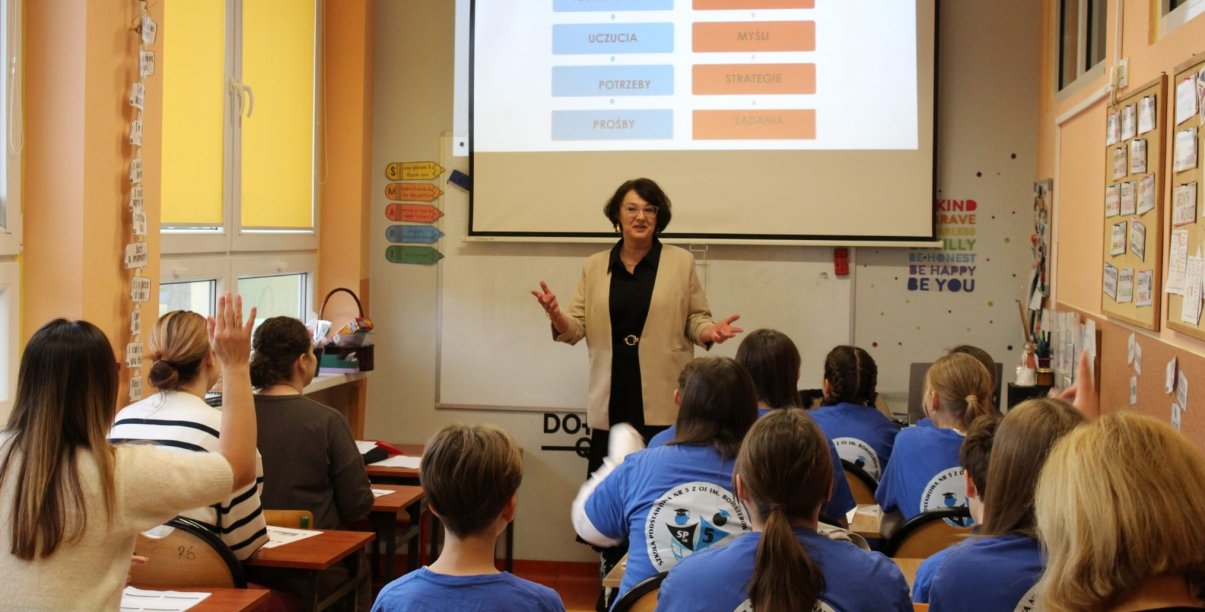 Uczniowie w ławkach przy tablicy kobieta prowadząca zajęcia