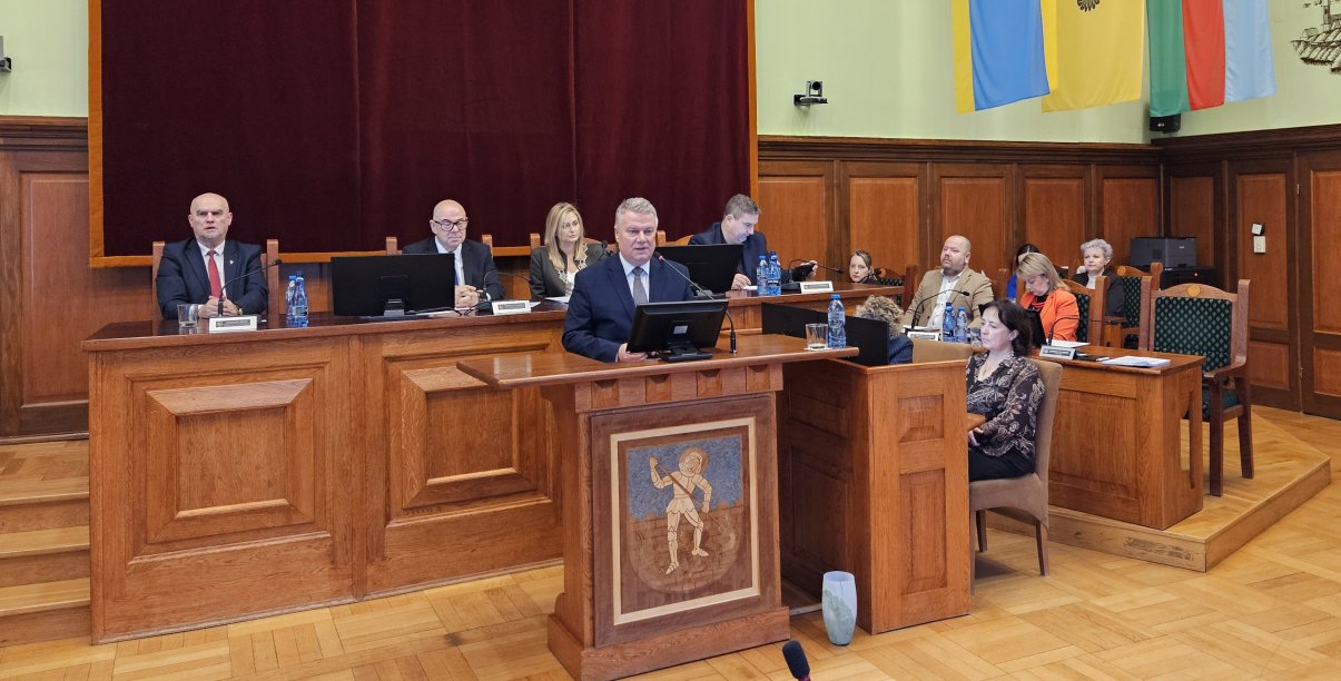 Burmistrz przy mównicy, za nim stół przy którym siedzi przewodnicząca i trzech wiceprzewodniczących