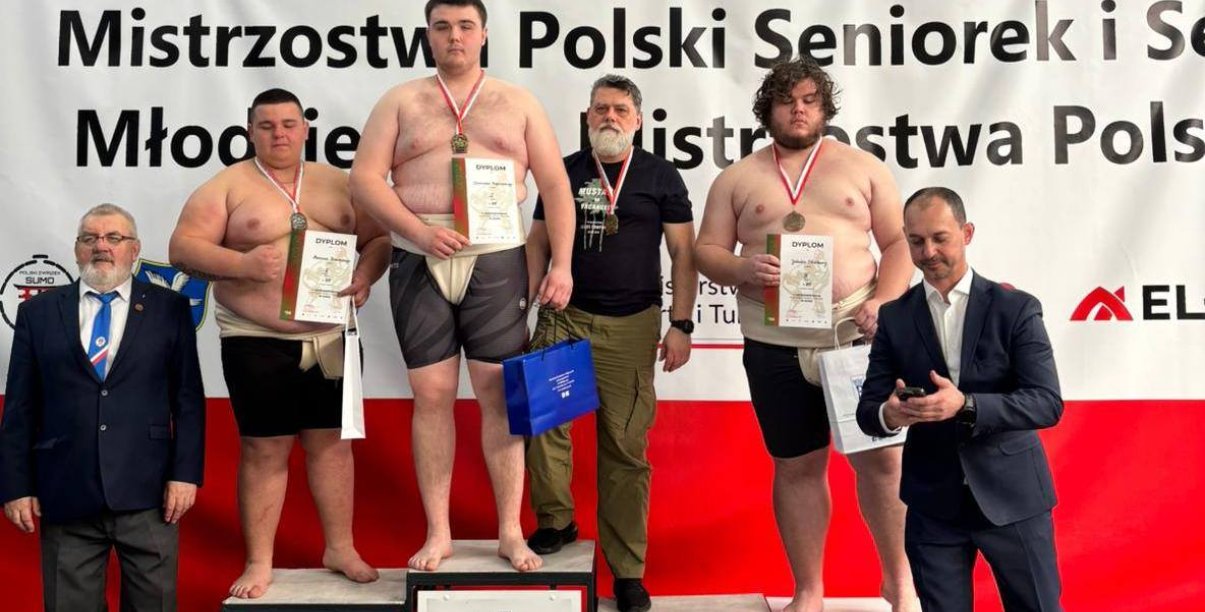 Zawodnicy sumo stojący na podium na biało-czerwonym tle