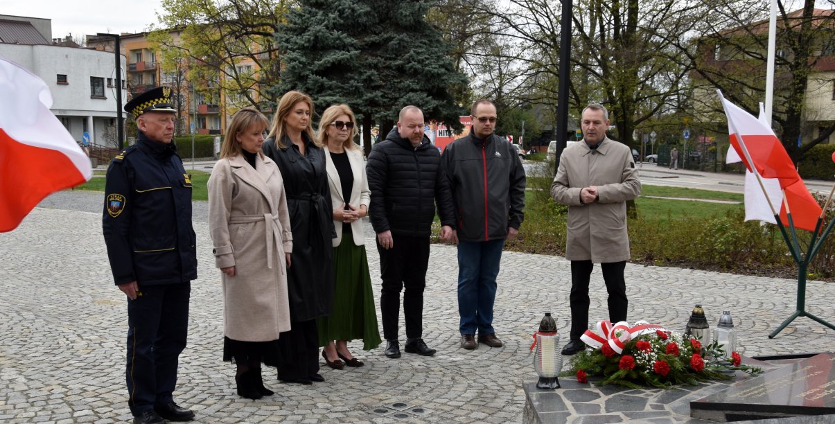 Trzy kobiety i czwórka mężczyzn stoją przed pomnikiem, po bokach flagi Polski