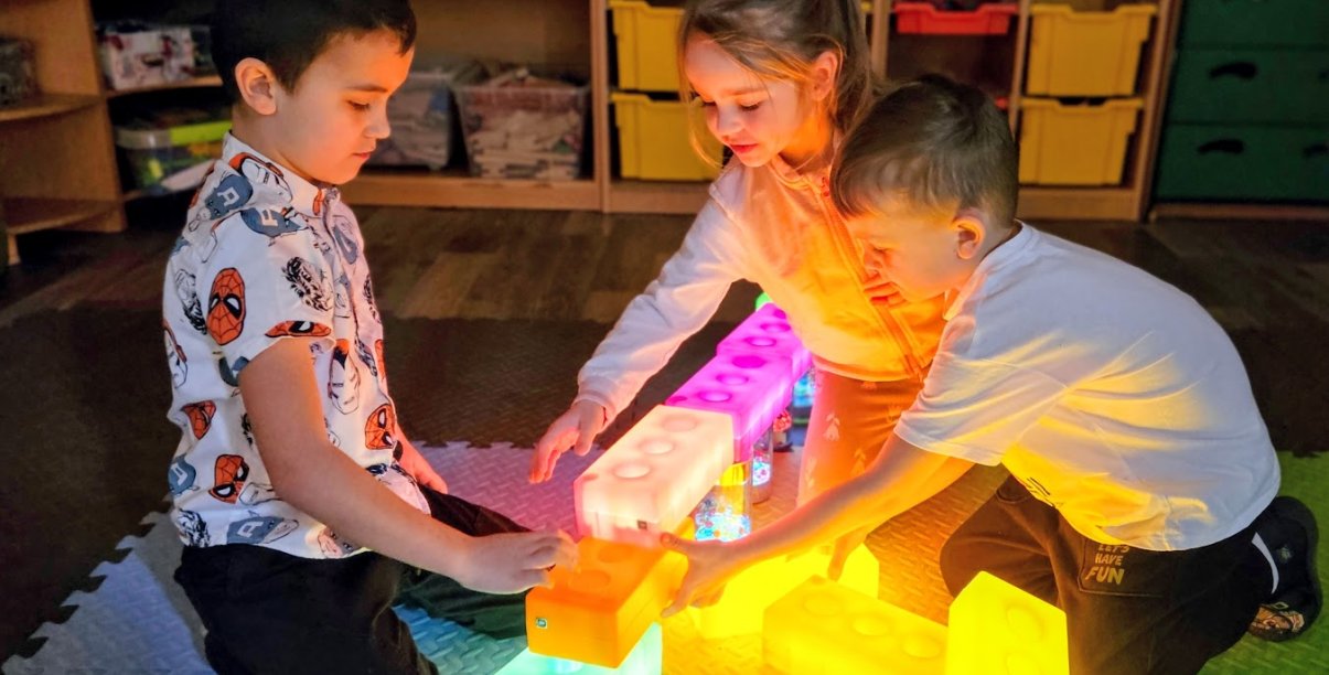 troje dzieci bawiących się świecącymi klockami